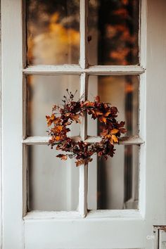 a wreath hanging on the front door of a house with autumn leaves in it's frame