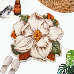 a white flower with green leaves is on the floor next to shoes and a straw hat