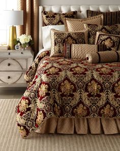 a bed with a red and gold comforter on top of it next to a white dresser