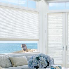 a living room filled with furniture and windows covered in white blinds next to the ocean