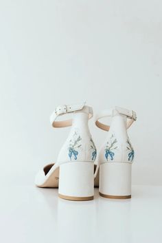 a pair of white high heeled shoes with floral embroidered on the front and back