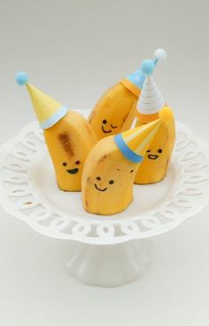 three bananas with party hats sitting on a cake plate