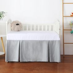 a white crib with a teddy bear on top and a gray bed skirt underneath