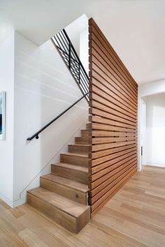 a wooden stair case next to a white wall and wood flooring in a house