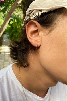 a close up of a person wearing a white shirt and earring with a tree in the background