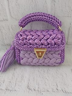 a purple handbag sitting on top of a white brick wall with a tasseled handle