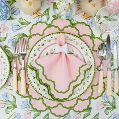 a table set with pink and green plates, silverware, and flowers on it