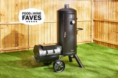 an outdoor charcoal smoker on wheels in front of a wooden fence and green grass