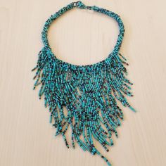 a blue necklace with beads and chains hanging from it's sides on a wooden surface