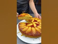 a person holding a piece of cake on top of a white plate with fruit toppings