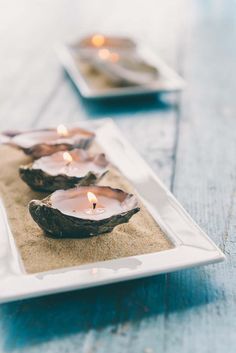 three seashells with lit candles in them on a plate sitting on a table