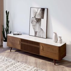 a white vase sitting on top of a wooden cabinet next to a painting and potted plant