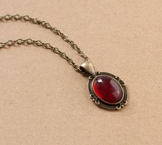 This beautiful Victorian style necklace is made from antique bronze chain and dark red cabochon housed in an ornate filigree setting. -the chain is 18 inches length -the pendant is approximately 1 inch long and 0.75 inch wide including the setting -lobster claw closure SHIPPING: Default shipping is by regular mail, which does not have tracking, shipping times are as follows: US: 1-2 weeks Canada: 1-2 weeks Europe: 2-3 weeks If you would like to add tracking for your parcel, please upgrade to Exp Red Jewel Necklace, Red Jewelry With Antique Finish As A Gift, Red Antique Finish Jewelry As Gift, Red Antique Finish Jewelry For Gift, Vintage Necklace Aesthetic, Red Antique Finish Jewelry Gift, Antique Red Pendant Jewelry, Dark Red Jewelry, Red Vintage Necklace With Cabochon