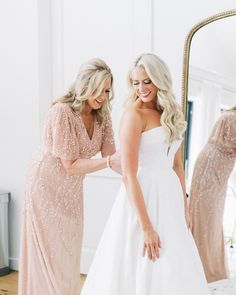 two women in wedding dresses looking at each other's reflection in a large mirror