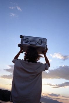 a woman carrying a suitcase on her head while standing in front of the ocean at sunset