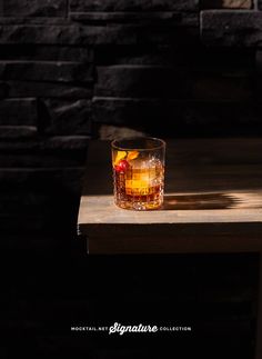 a glass filled with liquid sitting on top of a wooden table next to a brick wall