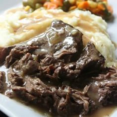 a white plate topped with meat and gravy covered in gravy next to mashed potatoes