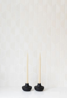 two white candles sitting next to each other on top of a table in front of a tiled wall