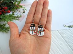 a hand holding two christmas themed earrings on it's left and the other one has a snowman