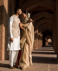 a man and woman standing next to each other in front of a brick building with arches