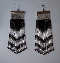 two pairs of black and silver beaded earrings hanging from hooks on a white surface