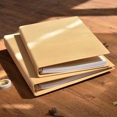 three binders sitting on top of a wooden table next to a roll of tape