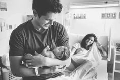 a man holding a baby in his arms while another woman watches from the hospital bed