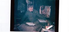 a man sitting on the floor in front of an easel and bookshelf