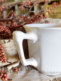 a white coffee cup sitting on top of a table next to some red berries and branches