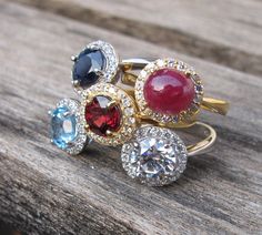 Halo Rings in Garnet, Blue Topaz, Blue Sapphire, Ruby. Create your Halo Ring with Belesas info@belesas.com Ruby Rings With Diamond Accents, Dazzling Round Crystal Ring With Accent Stones, Round Ruby Rings With Diamond Accents, Ruby Ring With Accent Stones, Garnet Birthstone Ring With Round Cut For Promise, Sapphire Ring With Gemstone Accents For Anniversary, Ruby Ring With Diamond Accents, Sapphire Ring With Cubic Zirconia And Gemstone Accents, Ruby Birthstone Ring With Gemstone Accents