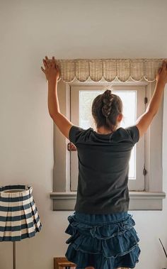 a woman standing in front of a window with her hands up and looking out the window