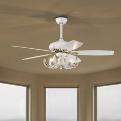 a white ceiling fan with four lights in a living room next to two large windows