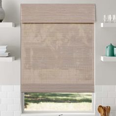 a kitchen window with roman blinds in the shade and dishes on the counter behind it