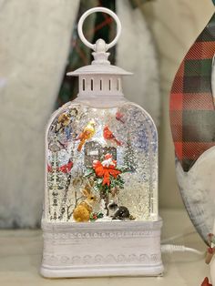 a snow globe with birds and flowers in it sitting next to a christmas ornament