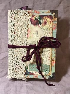 an altered book with lace and ribbon tied around the edges on a purple sheet of paper