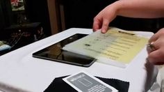 a person is holding an electronic device at a table with a menu and napkin on it