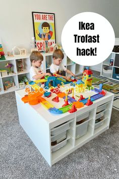 two young boys playing with toys in a playroom that is filled with storage bins