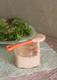 there is a small jar with something in it next to a salad on the table