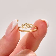 a woman's hand holding a gold ring with an arrow on the front and two leaves on the back