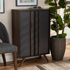 a tall wooden cabinet next to a gray chair and potted plant in a living room