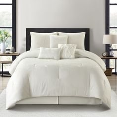 a bed with white comforter and pillows in a room next to two lamps on either side of the bed