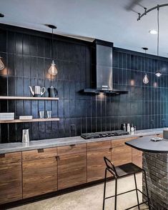 a kitchen with an island and bar stools next to the counter top, in front of black tiled walls