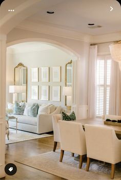 a living room filled with white furniture and lots of mirrors on the wall above it