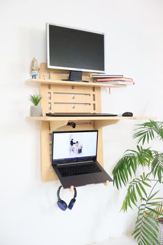 a laptop computer sitting on top of a wooden shelf next to a potted plant