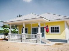 a small yellow house with a flag on the front porch and white railing around it