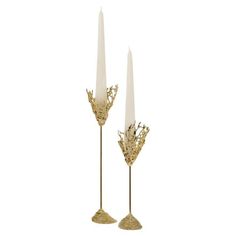 two tall candles sitting next to each other on top of a white surface with gold decorations