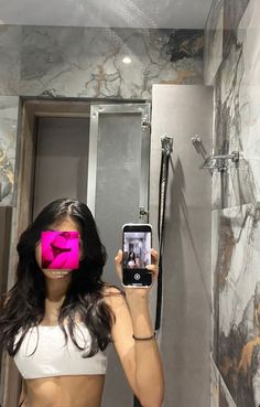 a woman taking a selfie in the bathroom with pink tape on her face and phone