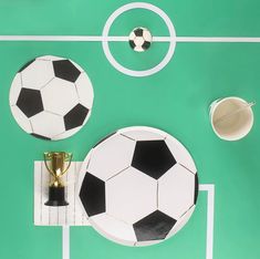 two soccer balls and a trophy on a green tablecloth with white lines in the background