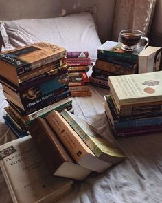 a pile of books sitting on top of a bed next to a glass of wine