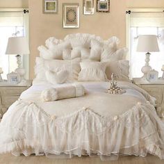 a bed with white ruffled bedspread and pillows on it in a bedroom